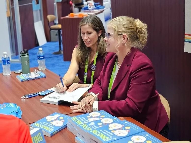Jenny Radesky and Megan Moreno at a table, signing copies of Connecting