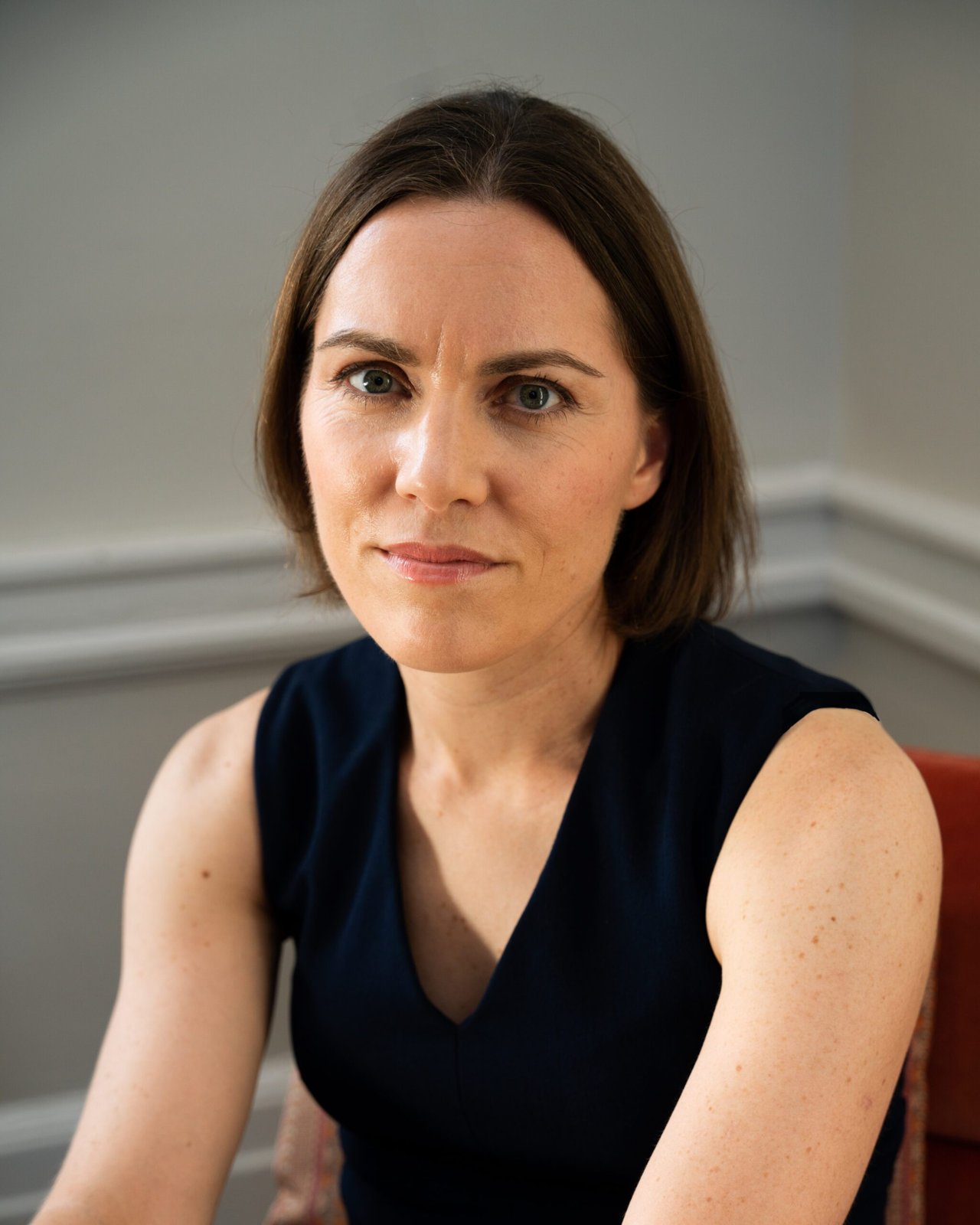 Emily Oster, an economist with short brown hair in a dark sleeveless top, sitting in a pale gray room