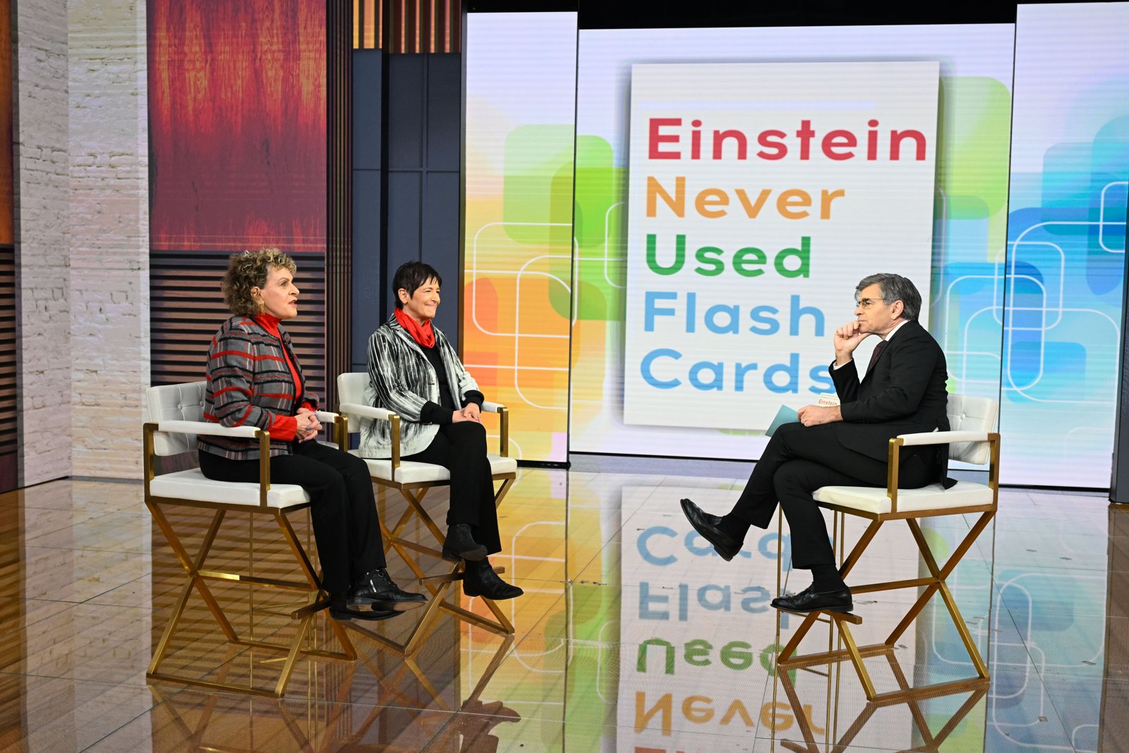 Kathy Hirsh-Pasek and Roberta Michnick Golinkoff sitting with George Stephanopoulos on the Good Morning America set, a large Einstein Never Used Flash Cards sign behind them