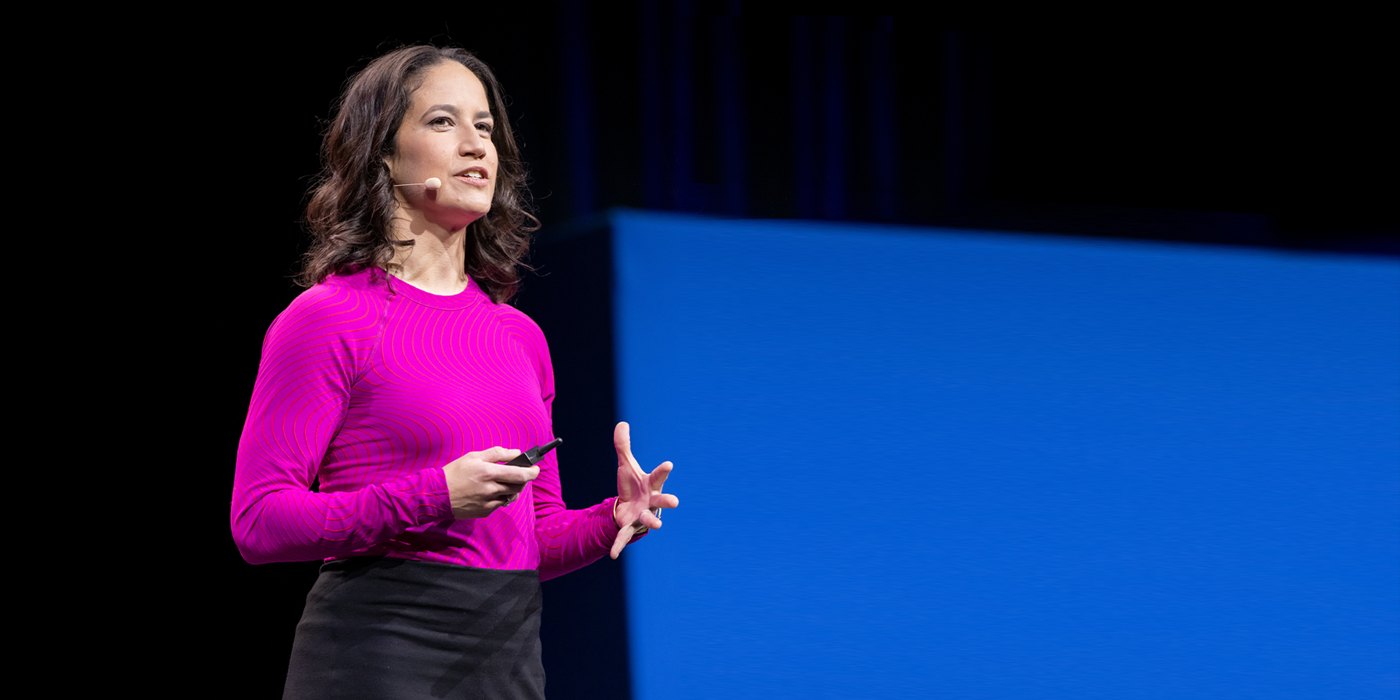 Catherine Price speaking on a dark stage in a bright pink sweater, with a blue screen behind her