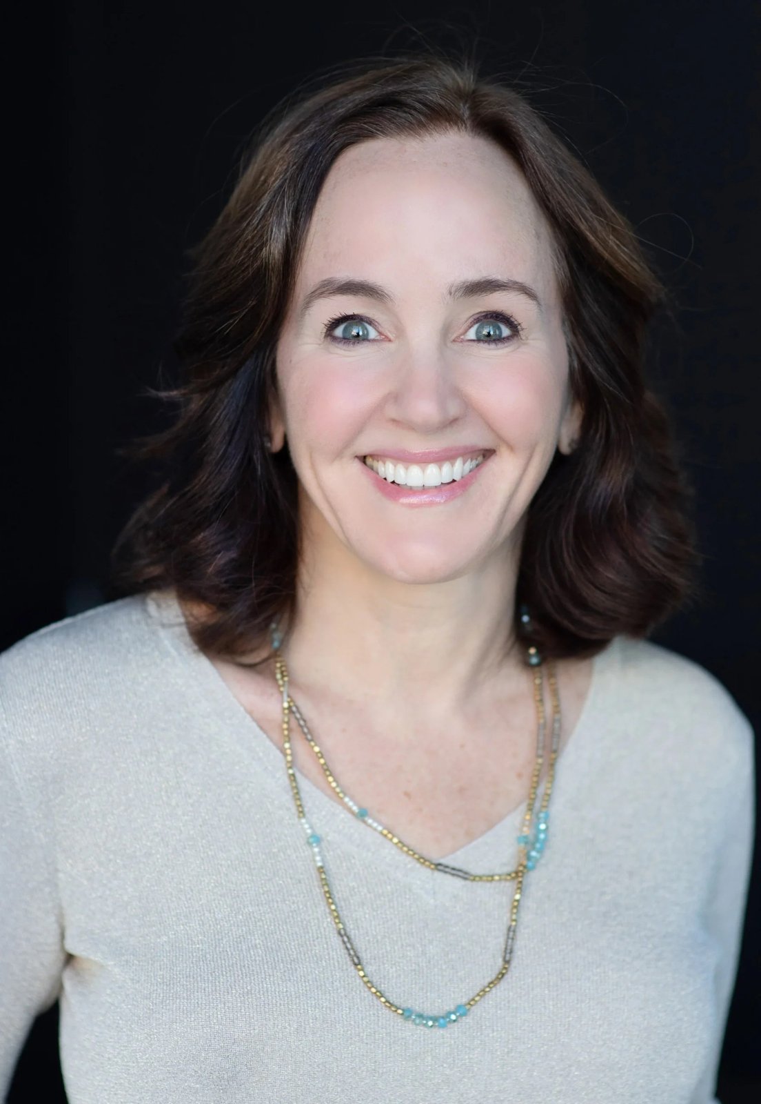 Dana Suskind, smiling, with shoulder-length brown hair and a long beaded necklace