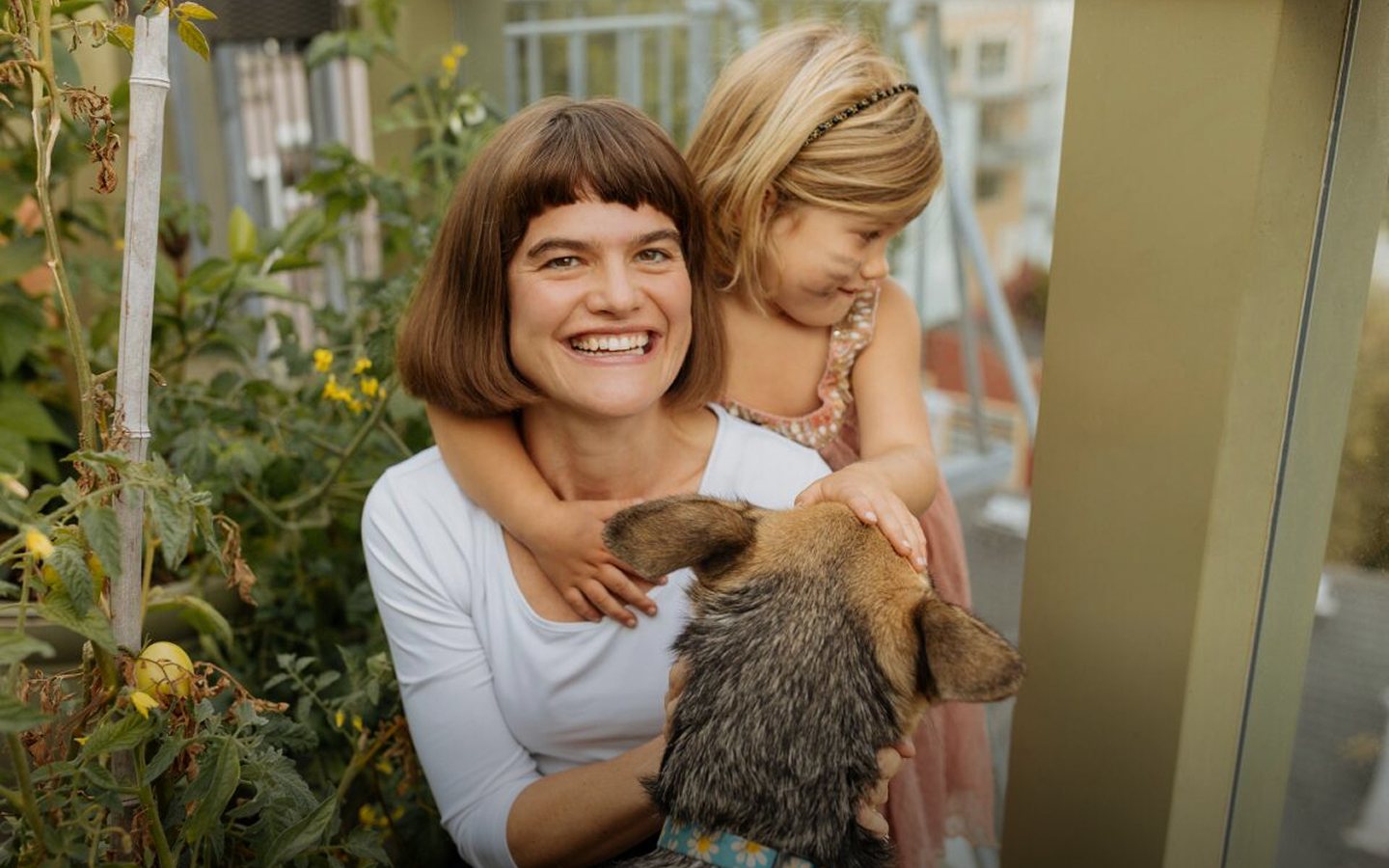 Michaeleen Doucleff smiling in a garden, her young daughter hugging her from behind and a shepherd dog in her arms