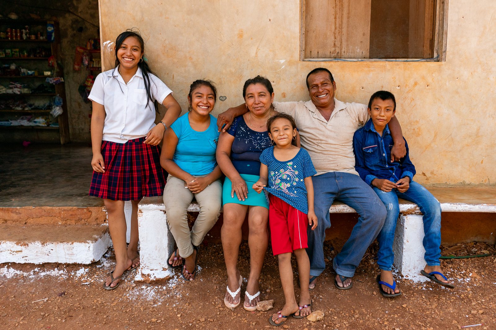 A Maya mother, father and four children sitting together on a bench outside their home, smiling