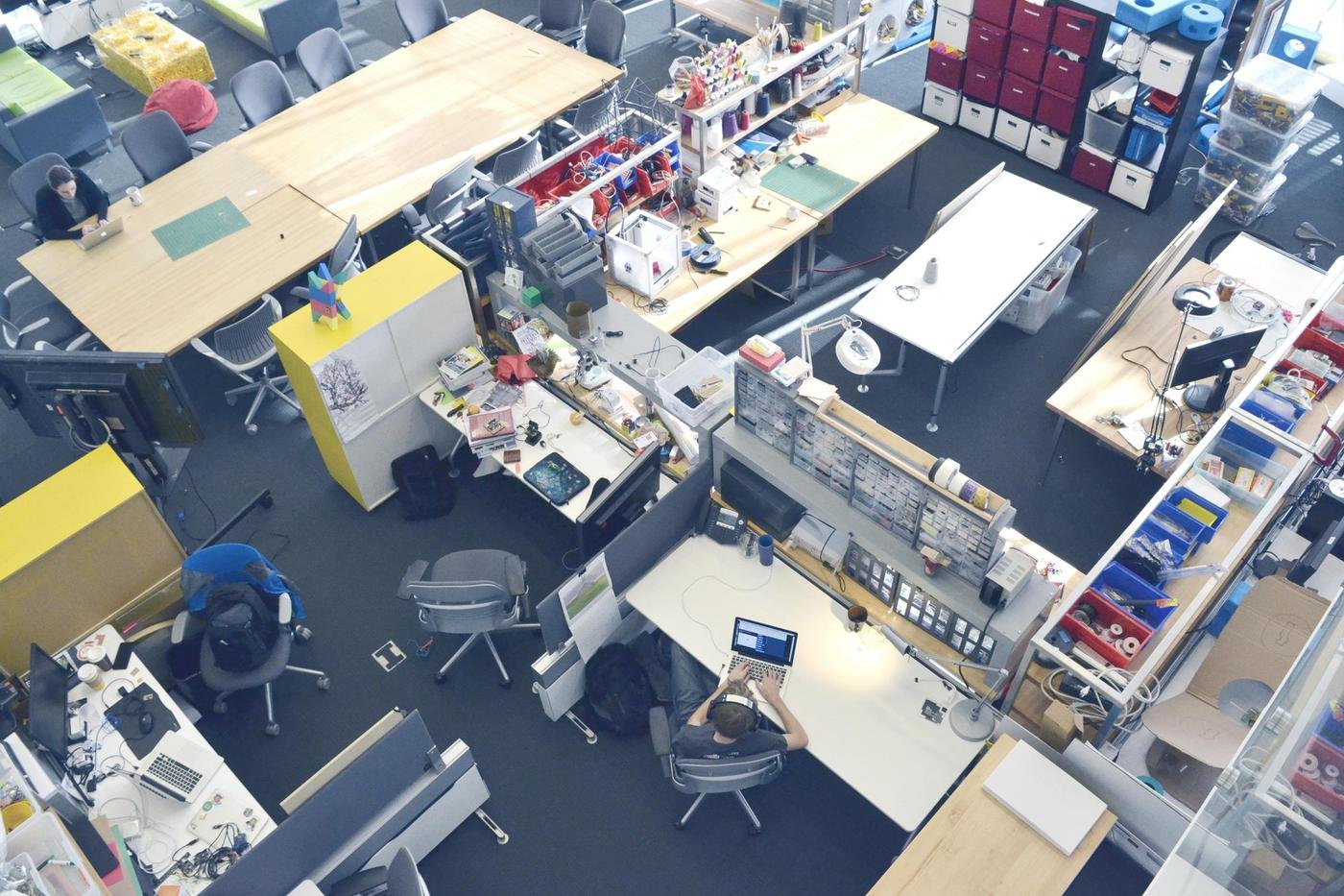 An overhead view of the Lifelong Kindergarten lab at MIT, with worktables covered in building materials, bins and laptops