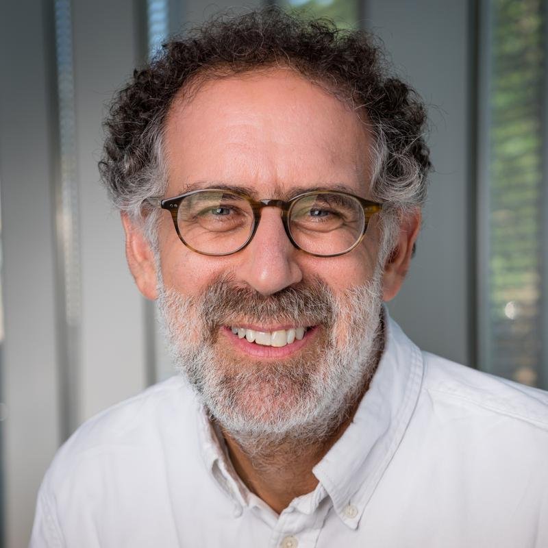 Mitchel Resnick, smiling, with curly gray hair, a beard and glasses, in a white shirt