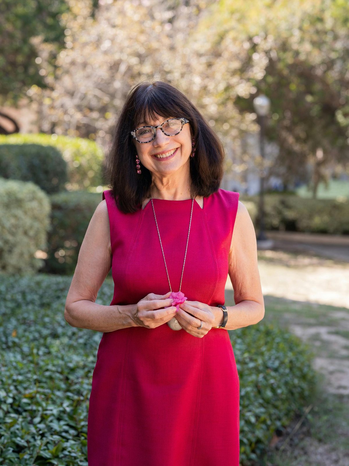Maryanne Wolf smiling in a red dress on a garden path on the UCLA campus