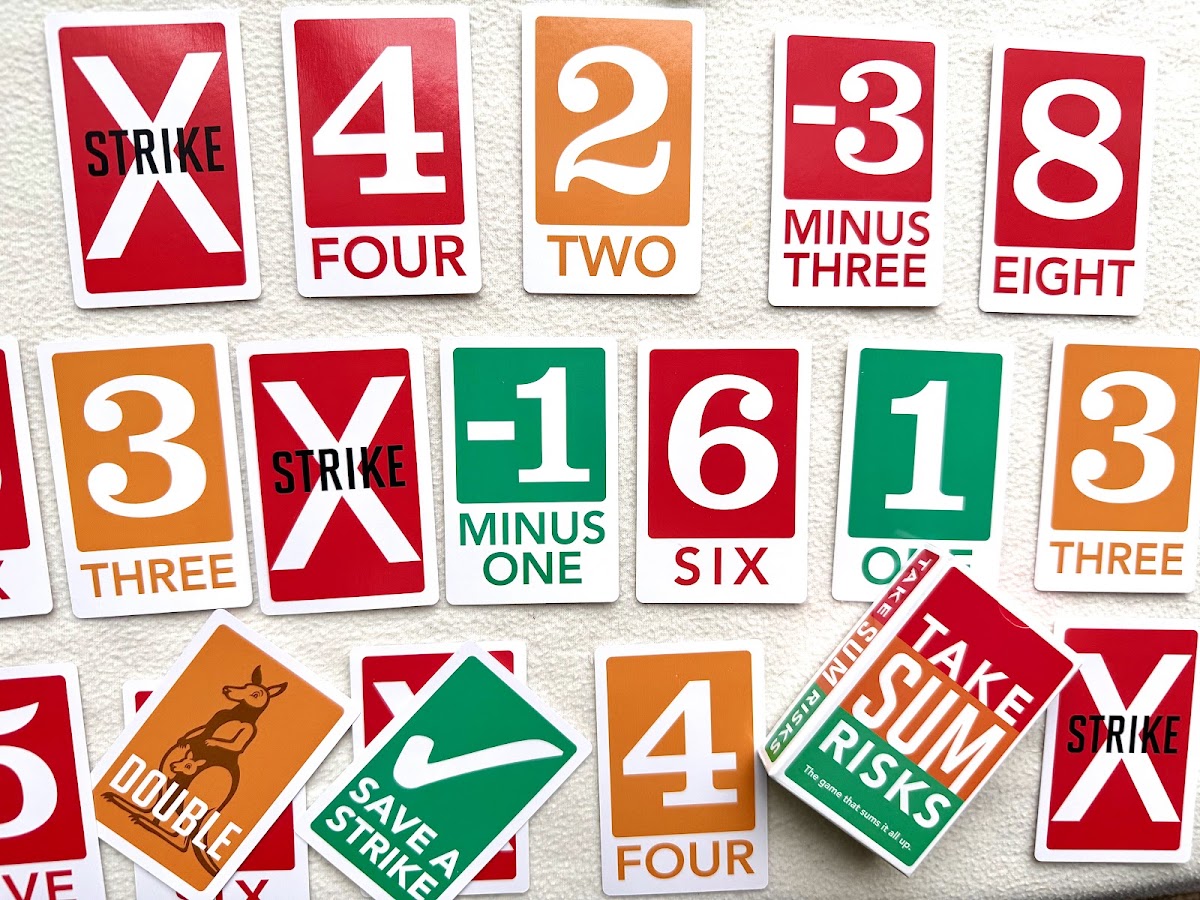 Take Sum Risks cards face up: Strike cards with a big X, red, orange and green number cards, Minus One, Minus Three, a Double card with a kangaroo and a green Save a Strike card
