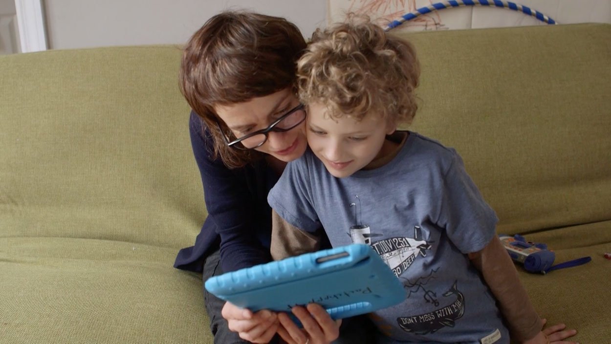 A mother and her young son on a couch reading a story together on a tablet in a blue case