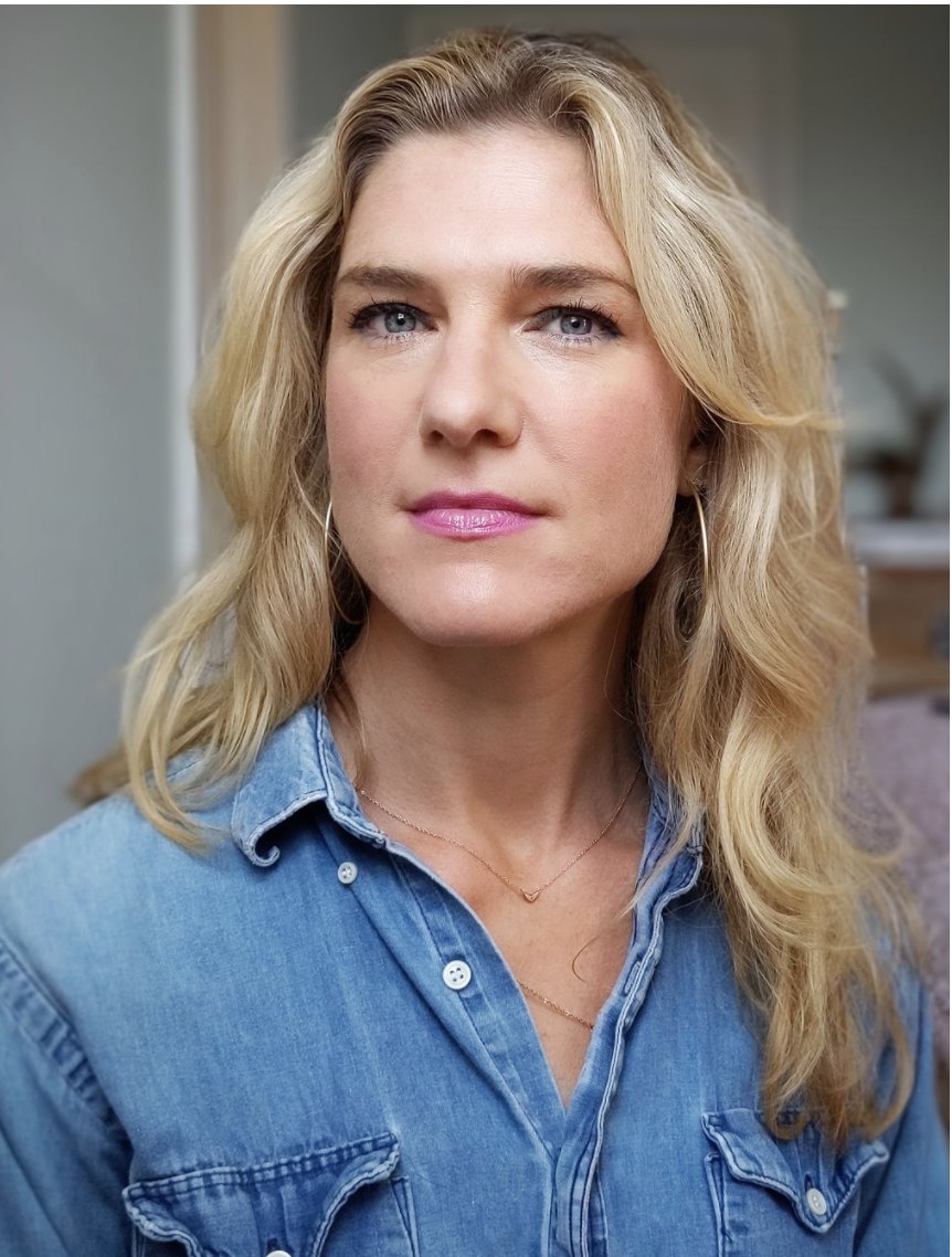 Anya Kamenetz with long wavy blonde hair, in a denim shirt, looking at the camera