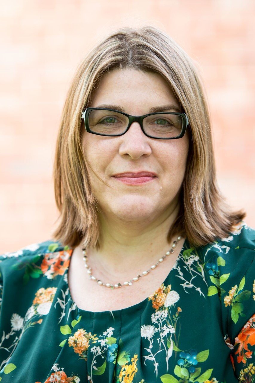 Donalyn Miller smiling in glasses and a floral top in front of a brick wall