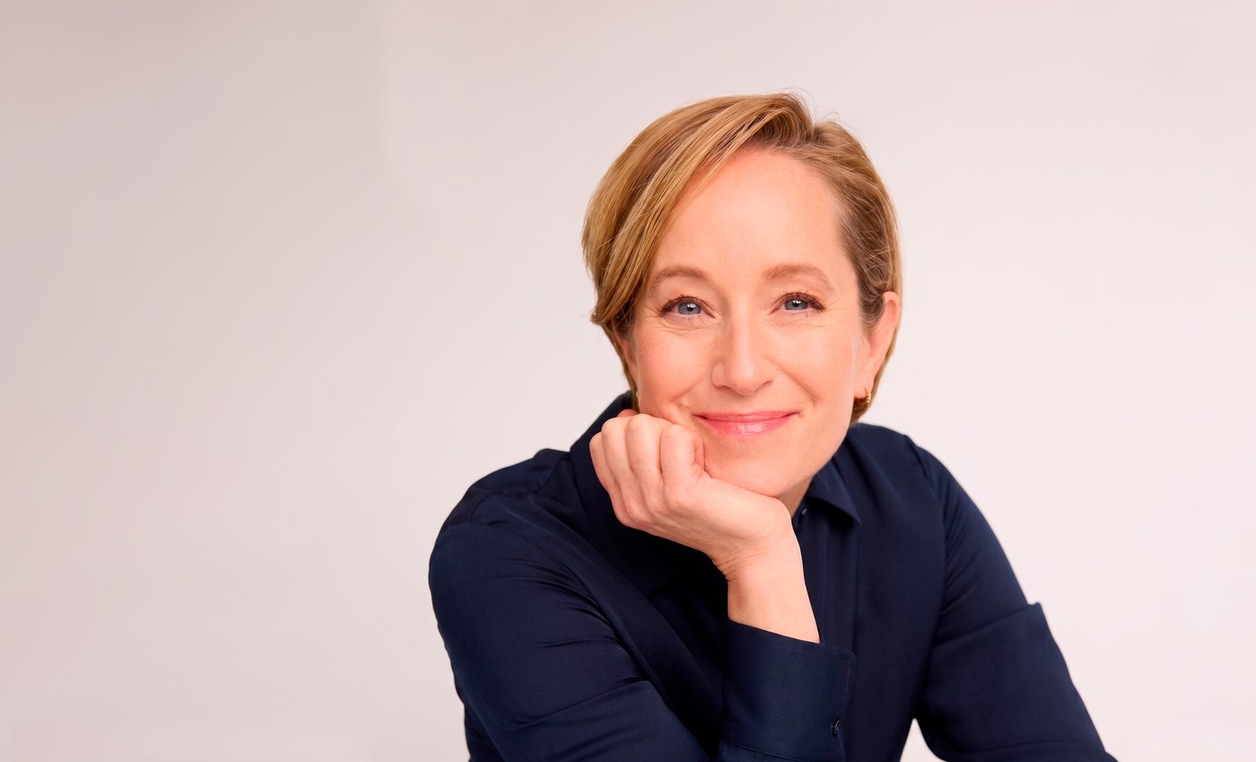 Psychologist Lisa Damour smiling with her chin resting on her hand, in a navy shirt against a pale background