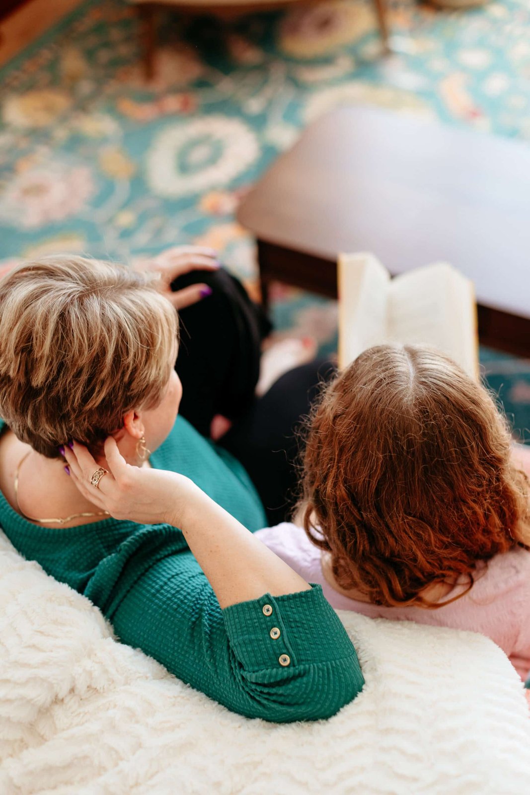 A mother and daughter on a couch, seen from behind, looking at an open book together