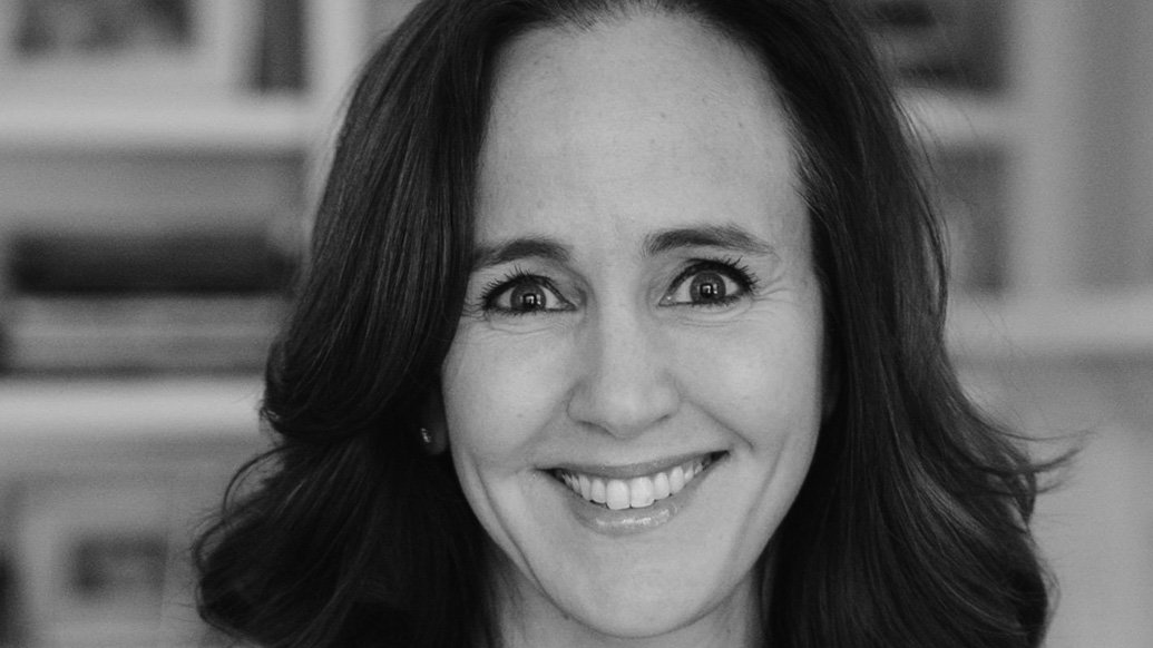 A black-and-white portrait of Dana Suskind smiling in front of a bookshelf