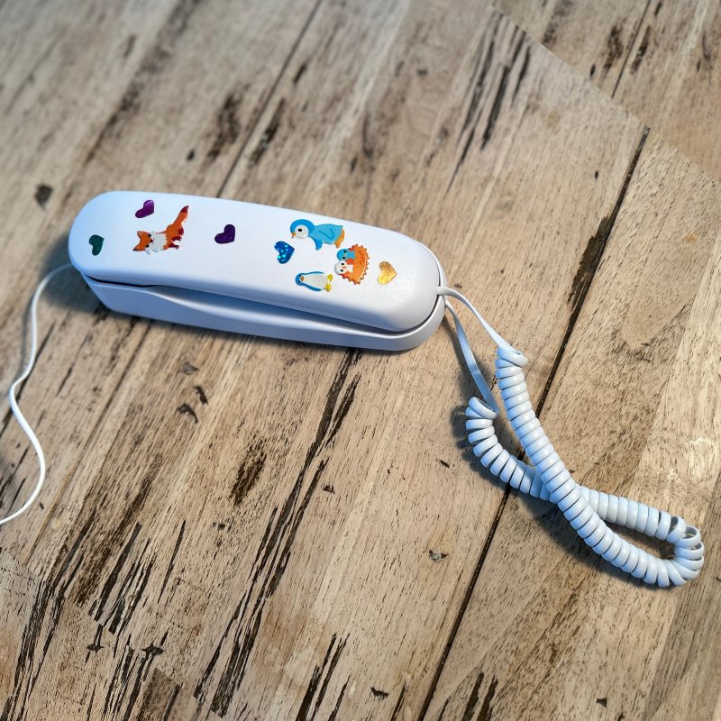A white Pinwheel Home phone covered in fox, penguin and heart stickers on a wooden table